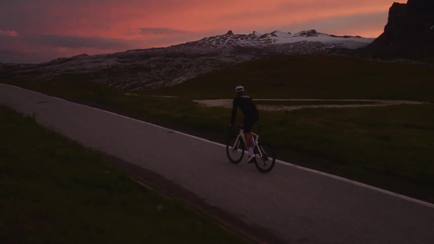 Man riding his bicycle on a mountain road under a red sunset sky