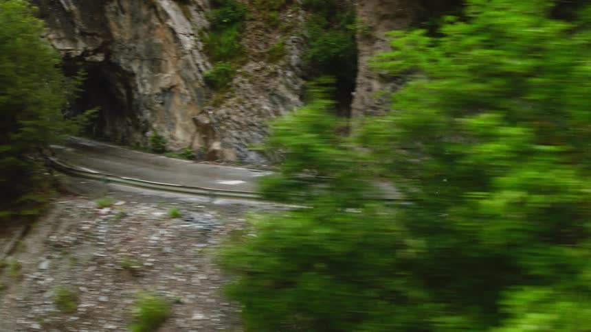 A view shows a person as they ride a bicycle along a winding road through a tunnel in a rocky cliff during the day