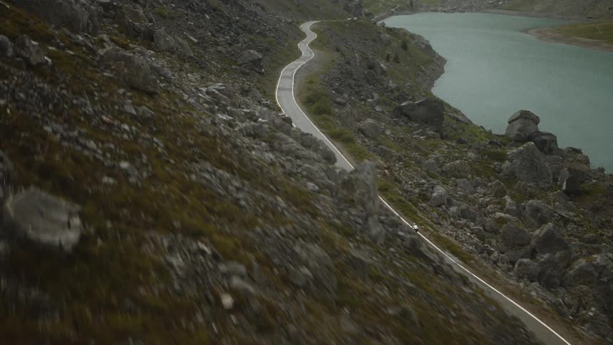 Cyclist rides along a narrow winding road on a rocky hillside near a lake