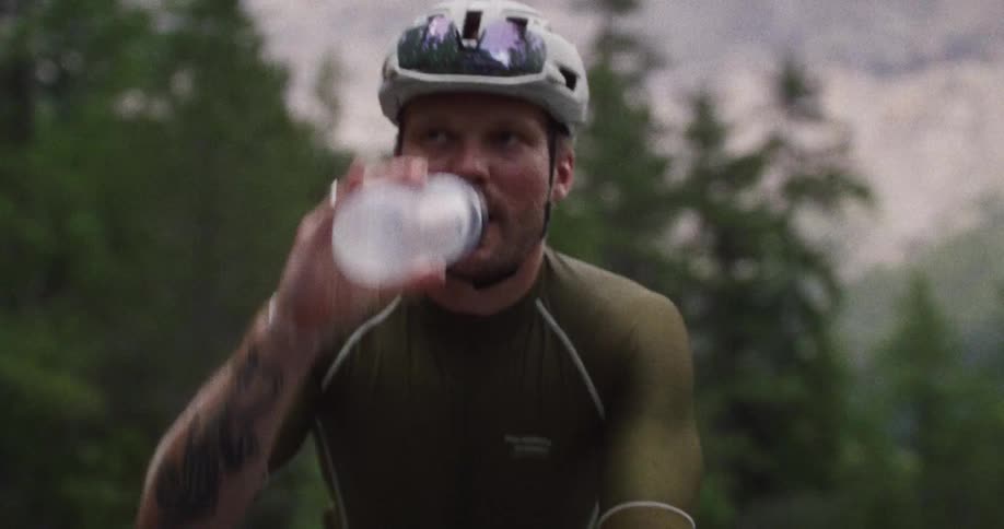 Cyclist wearing a helmet drinks and splashes water on his face while cycling in mountainous terrain