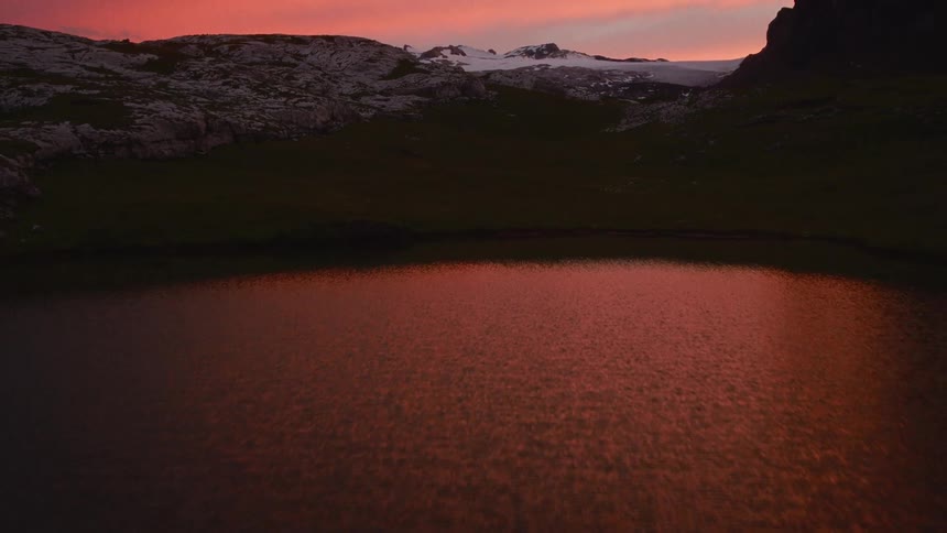 Mountain lake reflects an orange dusk sky with rocky terrain in the background