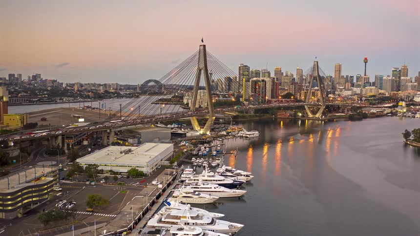 Cablestayed bridge over the river with a yacht marina in the foreground and an urban skyline in the background at dusk