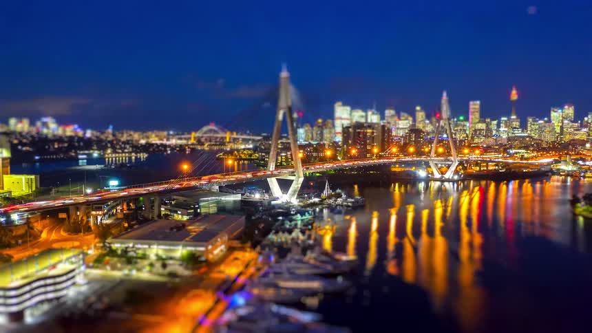 Vibrant city lights and traffic sparkle across an illuminated bridge in the nighttime harbor