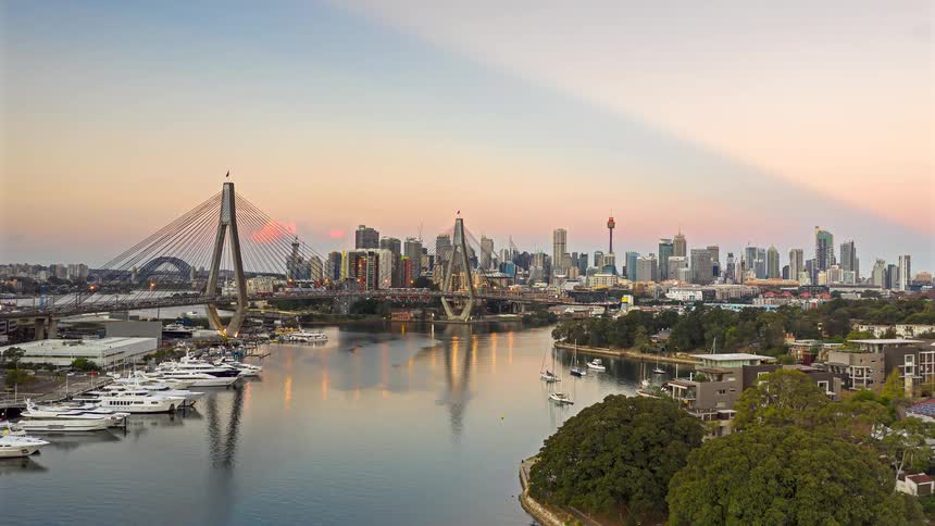 Cablestayed bridge crossing the river with a yacht marina on the left and an urban skyline in the background at dusk