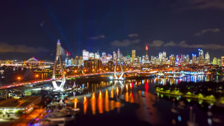 Illuminated cablestayed bridge over the river with reflections on the water and an urban skyline in the background at night