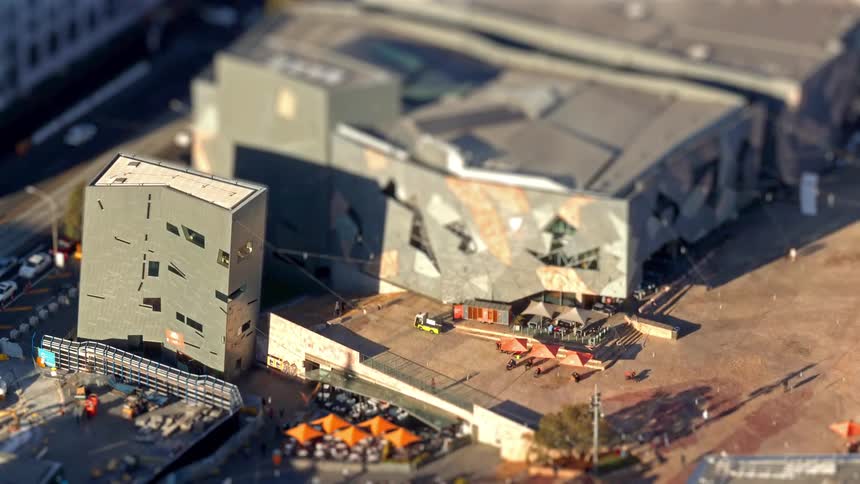 Aerial view of a modern metropolitan building complex with people and orange umbrellas in a city plaza
