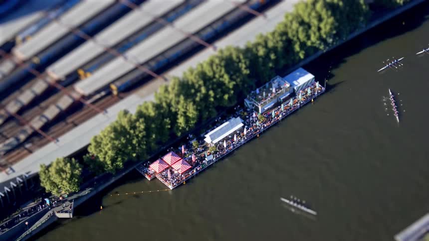 Audience watches rowing teams move through the water as a train passes nearby