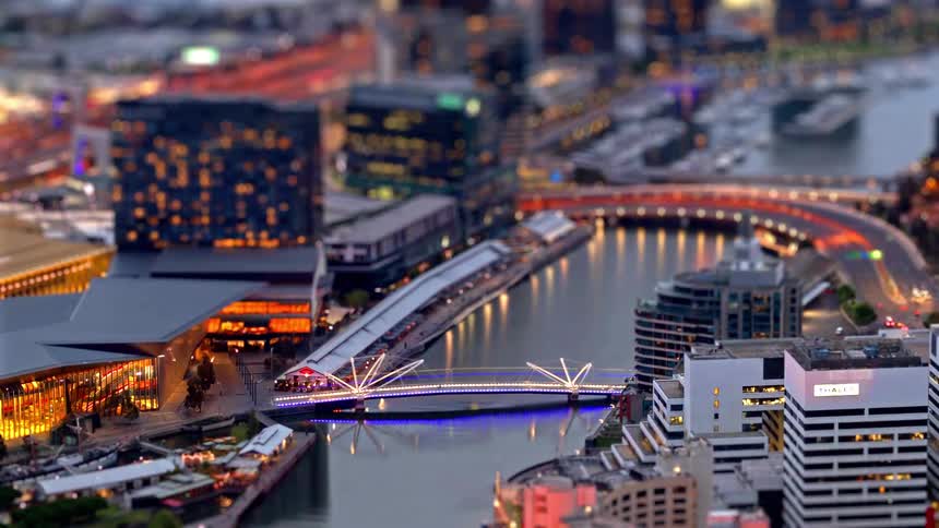 A glowing pedestrian bridge spanning a river surrounded by illuminated city buildings and streaks of traffic lights