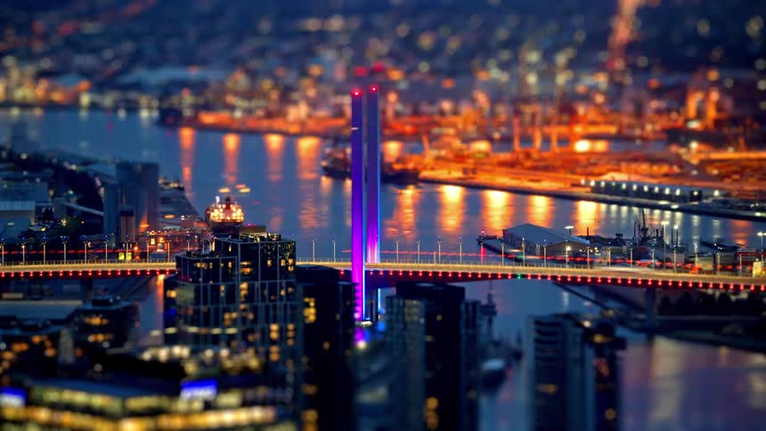 Traffic crosses a brightly lit bridge near the city as night falls