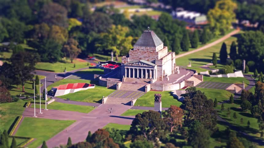 A view from above shows a large stone building with a pointed roof surrounded by green grass and trees during the day