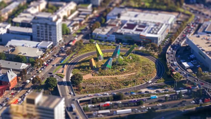 Urban roundabout with a central sculptural installation surrounded by traffic lanes and commercial buildings