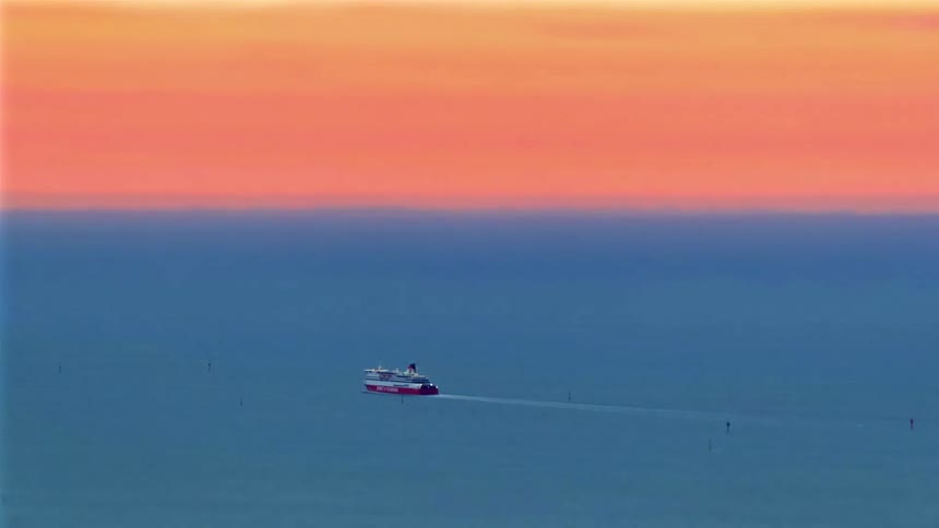A boat gliding over ocean water with the sky turning orange at sunset