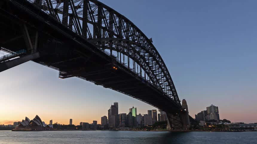 Arch bridge over the bay with an urban skyline and opera house in the background under early morning light