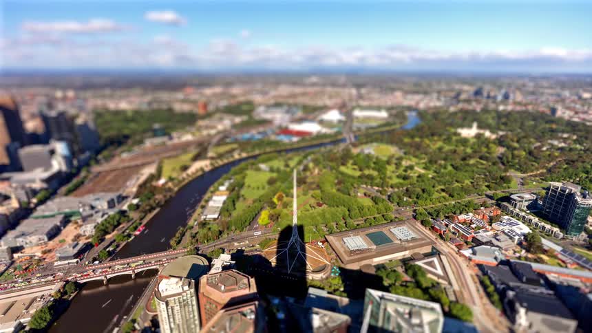 An aerial view of a city skyline and a river winding through the city next to green parklands and city buildings under a blue sky with clouds