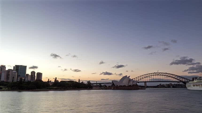 Sydney harbour in australia at sunset featuring the sydney opera house and the sydney harbour bridge transitioning into nighttime as boats and yachts move along the waterways