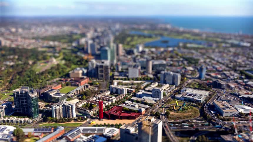 A bustling coastal city with dense highrises green parks and winding roads stretching toward the ocean