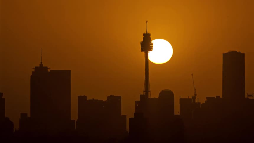 The city skyline is silhouetted against a golden sunset with lowering sun with a tall observation tower rising beneath the glowing sun