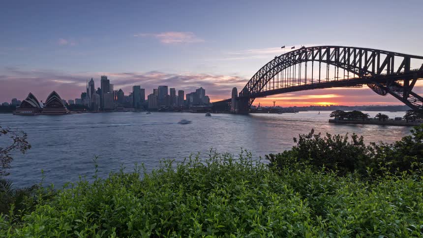 The city transitions from sunset into a glittering nightscape around the sydney harbour bridge and opera house