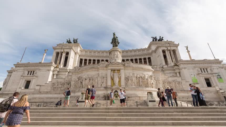 Historic monument with a wide staircase sculptures and visitors with italian flags flying under an open sky