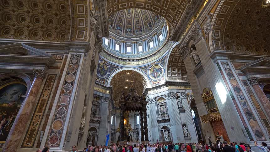 A grand historic cathedral with towering columns and ornate ceilings as tourists walk along the central nave
