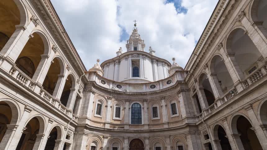 Symmetrical inner courtyard with twolevel arcades and a central domed building under a partly cloudy sky