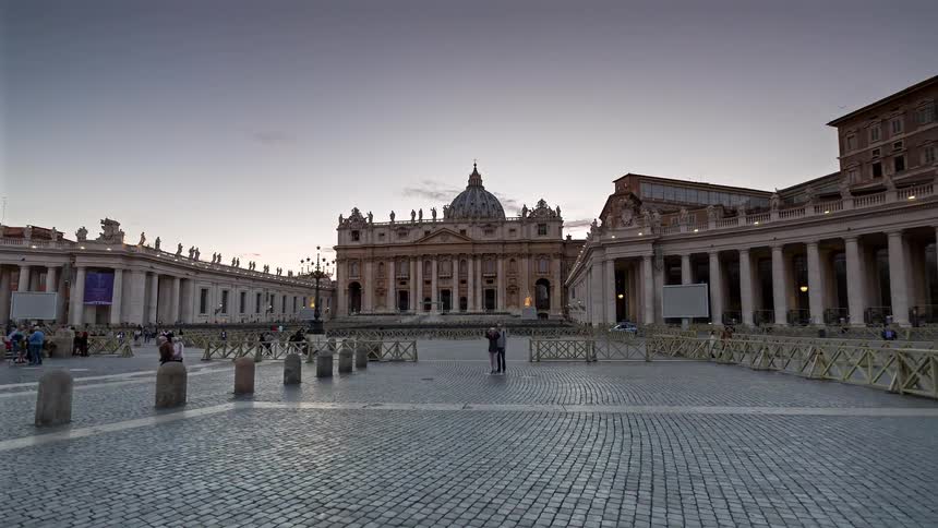 Tourists visiting and leaving st peters square as day turns to night with streetlights illuminating the surroundings