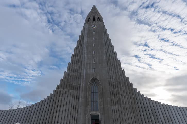 A large group of people walking to and fro in front of the hallgrmskirkja church at midday