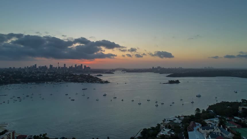 The sun sets over a city skyline and harbor as clouds drift through the evening sky