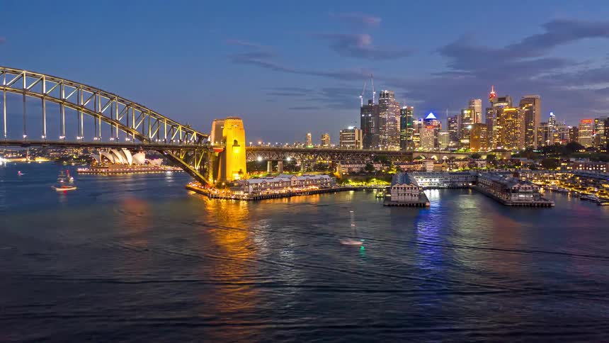 Sydney harbour bridge illuminated over the bay boats in motion and the city skyline in the background at night