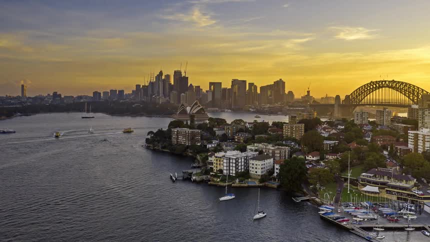 Boats sail in the harbor with a bridge and buildings along the coast and city skyline in the distance