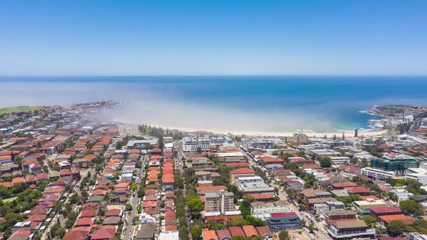 A city at midday filled with residential buildings and condos with an ocean view in the background