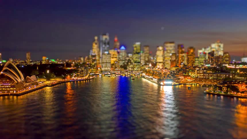 Night skyline of sydney with the sydney opera house on the left illuminated skyscrapers in the background and city lights reflected on the harbor water