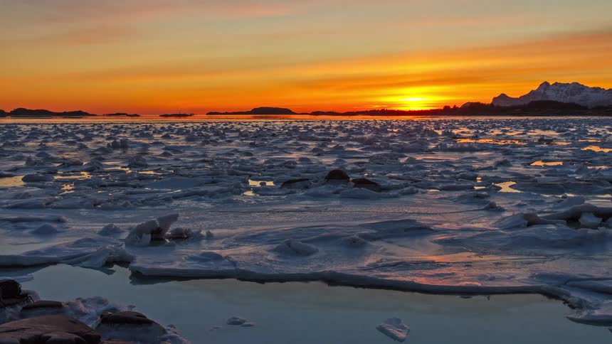 Arctic sunset on the horizon with ice floes drifting across the partially frozen sea