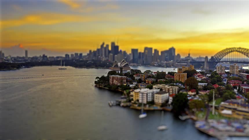 A miniature style aerial view captures sydney harbors iconic landmarks under a vibrant sunset sky