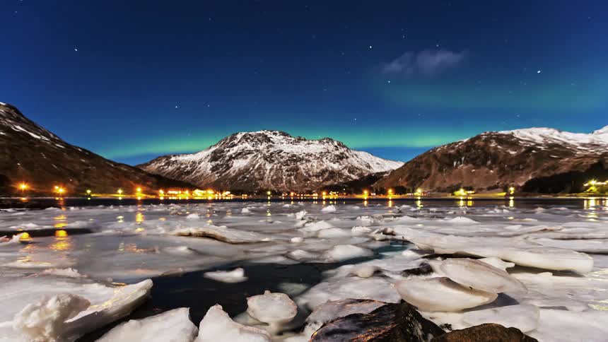 A series of ice formations floating on a river with a snowcovered mountain range along the riverbank at sunset