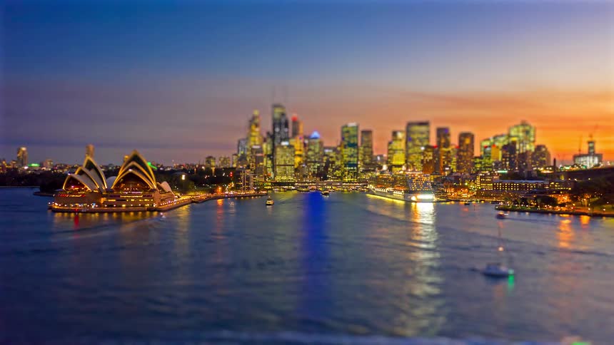 Aerial view of the sydney opera house and city skyline glowing over the harbor at dusk