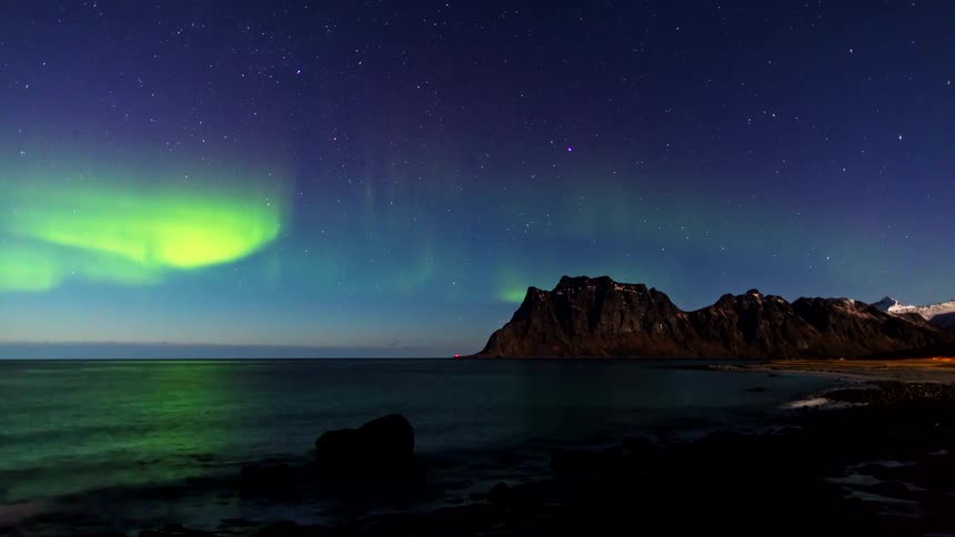Northern lights over the ocean with a coastal rock formation under a starry night sky