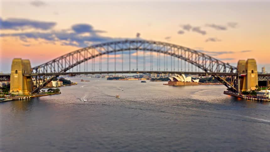 At sunset an arch bridge over a river with a series of ships moving to and fro beneath it