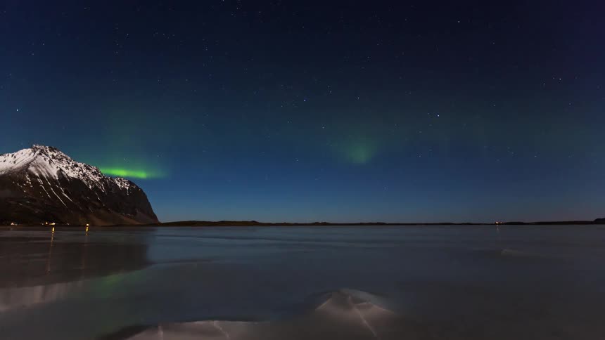 Faint aurora borealis in the night sky over a frozen lake with a snowcovered mountain on the left