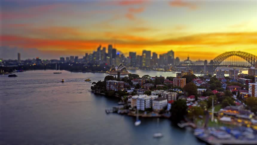 A toy like view of sydney harbor and its iconic landmarks glows under a vibrant orange sunset