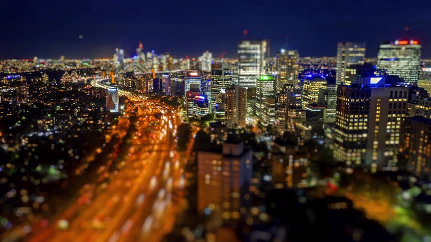 Night aerial view of an urban area with illuminated buildings and an expressway with heavy traffic