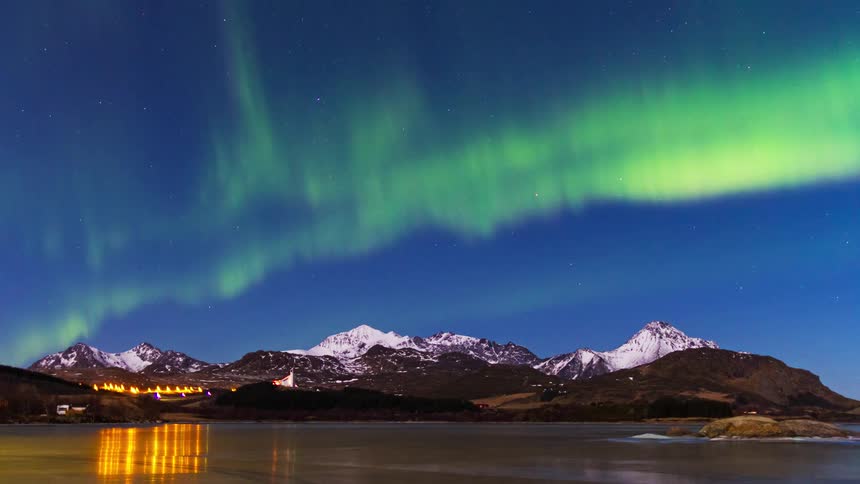Northern lights move over a mountain town on a lake
