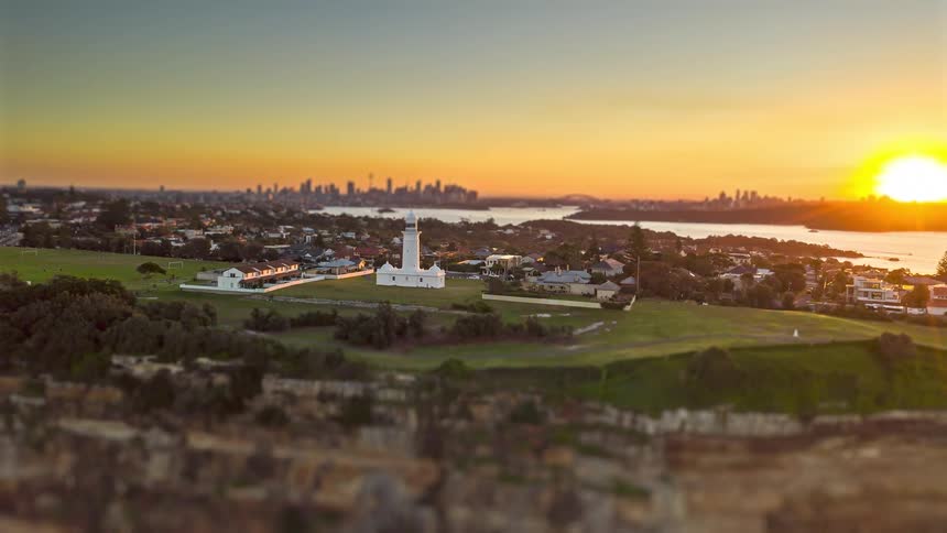 Aerial view of macquarie lighthouse and sydneys coastal homes at sunset with the distant skyline