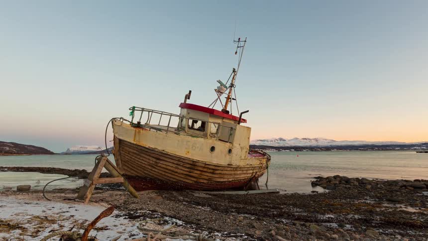Fishing vessel grounded on the shore with calm water and mountains in the background at dusk