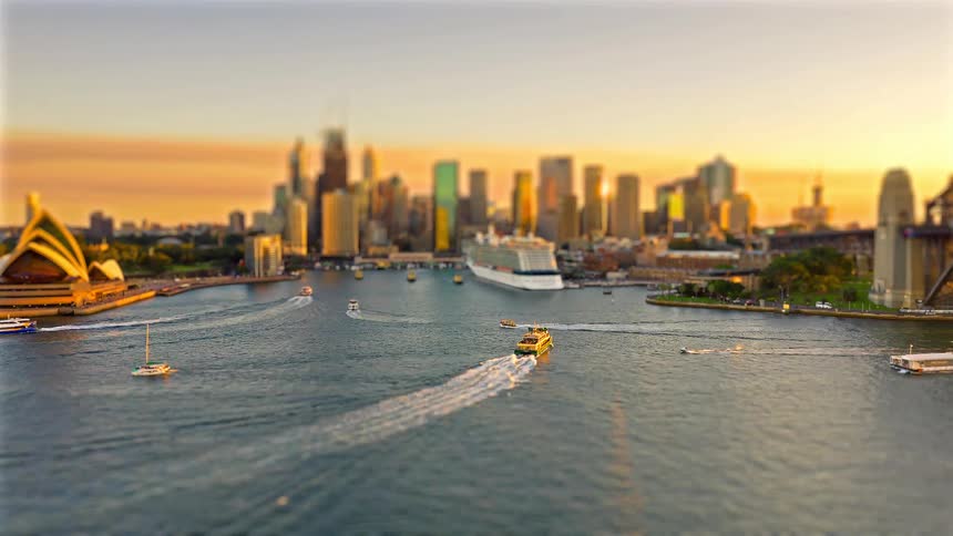 Bustling boats and ferries move through sydney harbor past iconic landmarks under a vibrant golden sunset