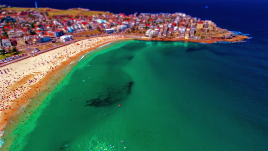 Coastal community with people on the beach and in the water as a small boat sails and waves roll in to shore