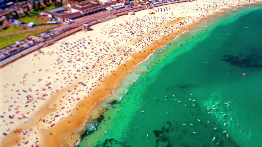 Coastal community with people on the beach and in the water as a small boat sails and waves roll in to shore