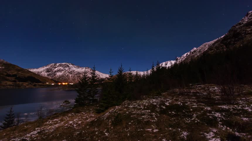 Headlights on an automobile glow as it travels on a road through the mountain river valley
