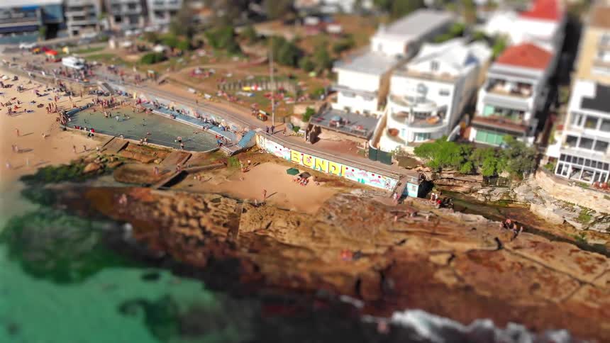 Many people walking on the streets and the beach of a busy coastal neighborhood with a swimming pool