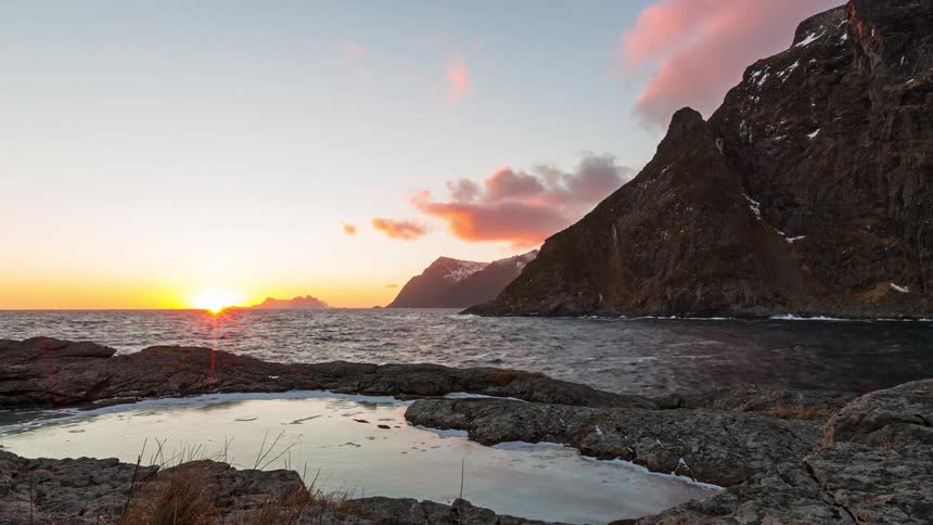 Rocky coastline with a natural tide pool in the foreground open sea and mountains in the background at sunset